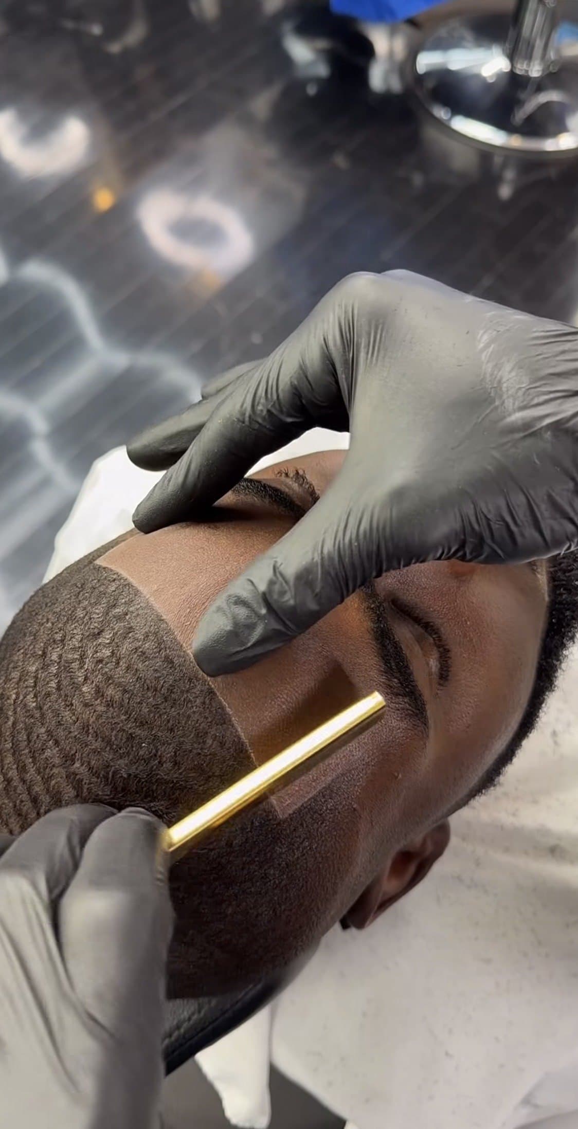 Barber traçant au rasoir le contour du front et de la barbe d'un client aux cheveux courts ondulés